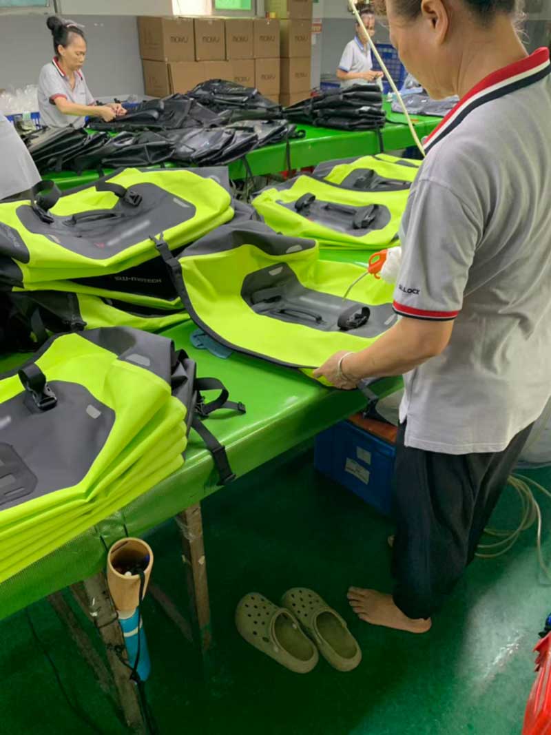 Worker inflating a finished waterproof motorcycle bag with an air line for leak testing
